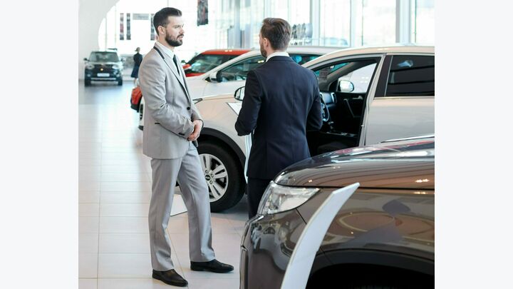 Professional salesperson selling new cars in a modern auto salon. Two men standing and choosing a new car