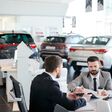 Bearded young male customer signing a contract for rent a car while sitting at car showroom