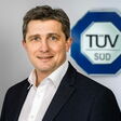 Gerald Bachler, neuer CEO von TÜV Süd für CEE mit Firmenlogo im Hintergrund