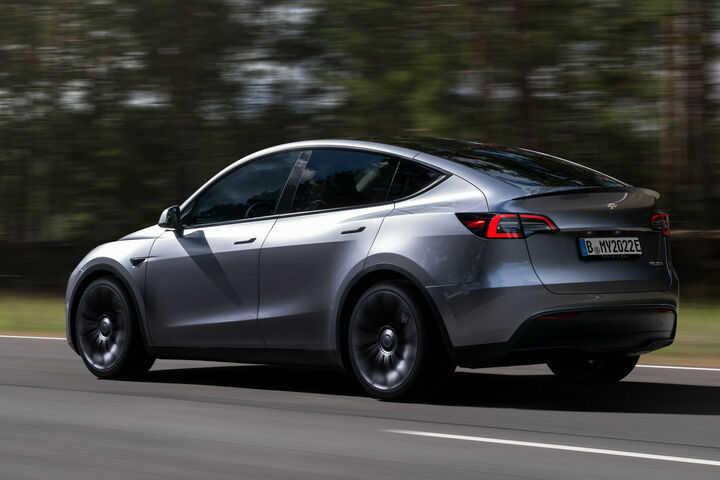 Tesla Model Y Metallic-Silber auf der Straße mit Wald im Hintergrund
