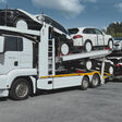 MAN Autotransporter in Weiß beladen mit Fahrzeugen auf einem Parkplatz.