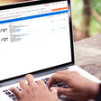 Stock Image of laptop with TecDoc database frontend composited onto the screen, sitting on the table in what appears to be a Forrest or jungle in the out of focus background.