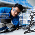 A young mechanic opens the hood of a car to check for engine damage and perform professional maintenance. He wears a blue uniform and inspects and repairs his car in the maintenance center.