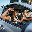 Two young women sing a song on the radio and dance in the car on a day trip in the summer - Best friends having fun together driving around the countryside - Smiling millennial in a relaxing moment