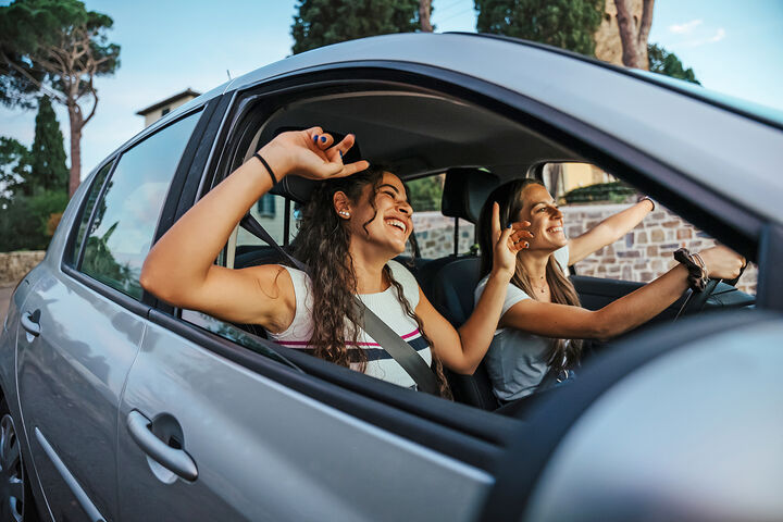 Two young women sing a song on the radio and dance in the car on a day trip in the summer - Best friends having fun together driving around the countryside - Smiling millennial in a relaxing moment